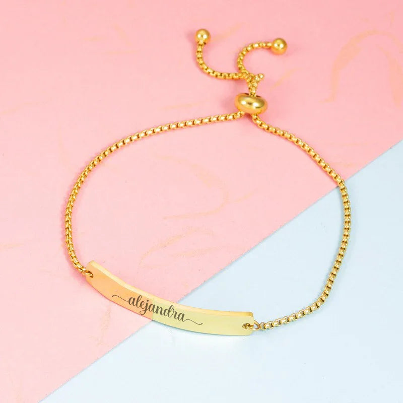 Pulsera dorada personalizada con nombre Alejandra, divertida y elegante sobre fondo rosa.