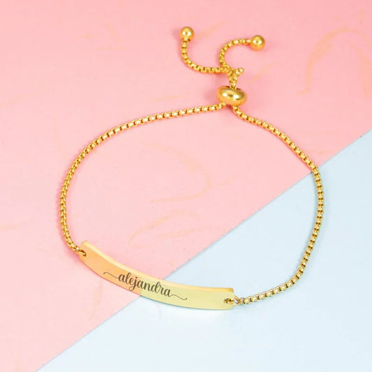 Pulsera dorada personalizada con nombre Alejandra, divertida y elegante sobre fondo rosa.