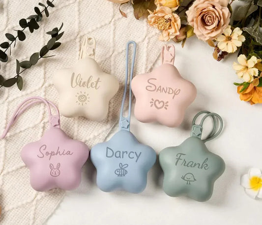 Portachupetes de silicona en forma de estrella, personalizados y coloridos, sobre manta con flores.